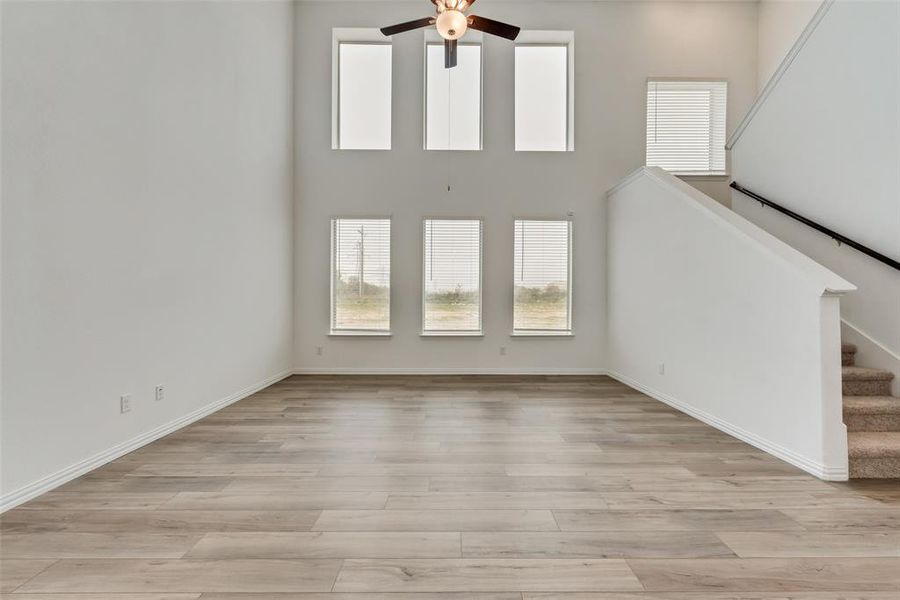 Unfurnished living room featuring light wood-type flooring, ceiling fan, and a towering ceiling