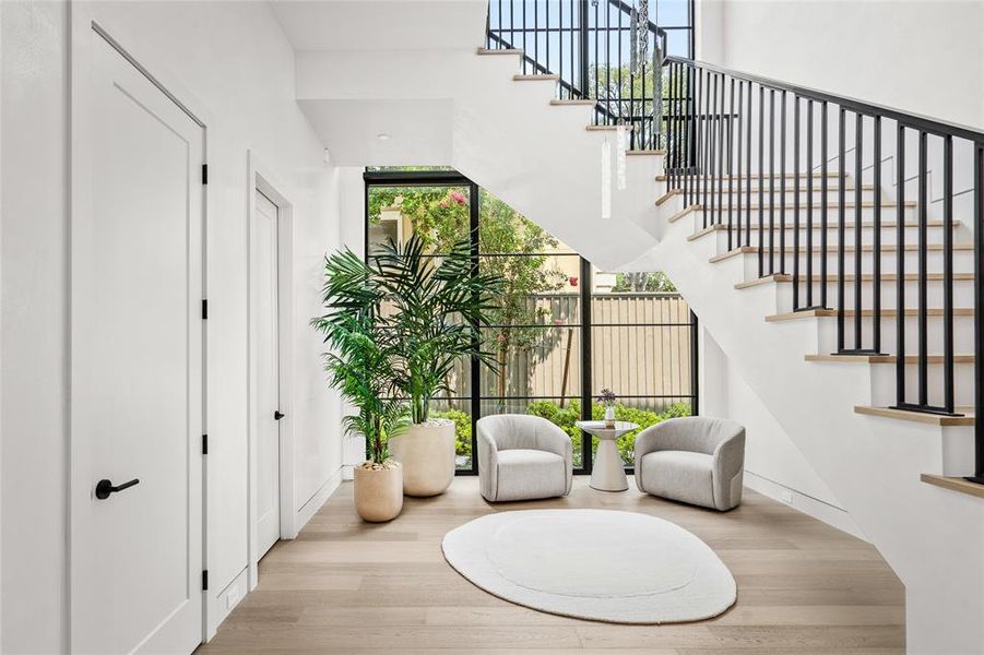 This versatile space offers room for an additional sitting area or a grand piano. To the left, you'll find the powder room and elevator. Expansive floor-to-ceiling windows flood the space with abundant natural light as the bespoke modern chandelier illuminates the area and a custom iron railing along the stairs gently usher you to the second floor.