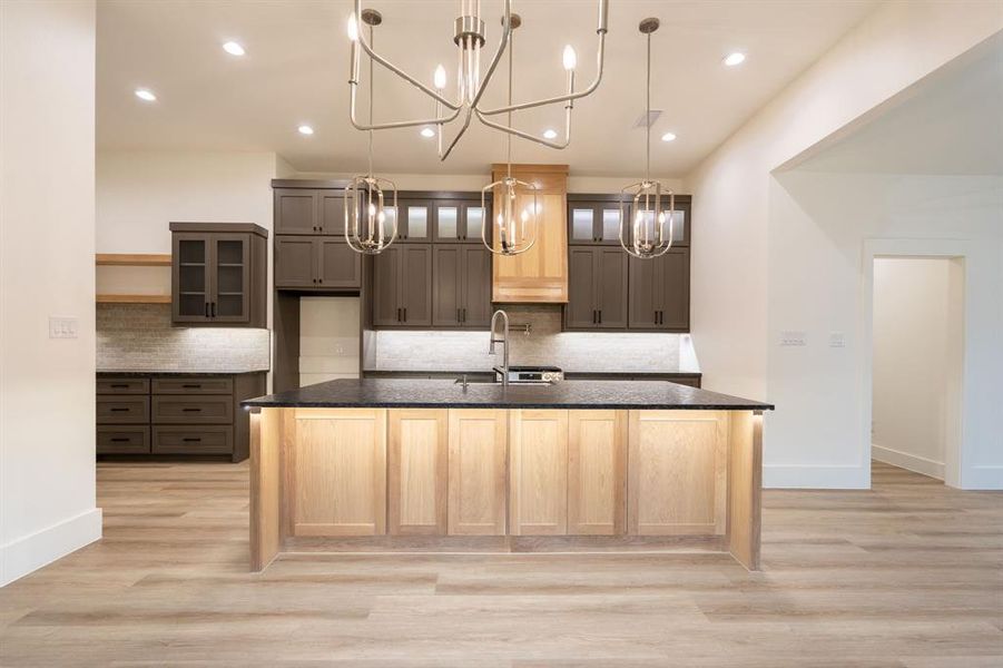 Kitchen featuring sink, a kitchen island with sink, backsplash, light hardwood / wood-style flooring, and dark stone countertops