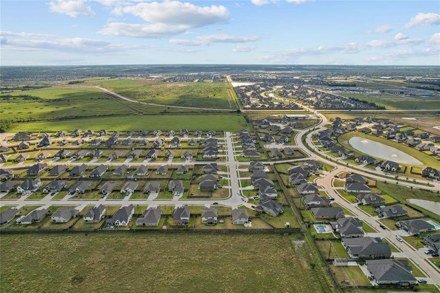 A wide-angle aerial view showing the home’s full exterior and large lot, nestled in a picturesque community with easy access to everything Mont Belvieu has to offer.