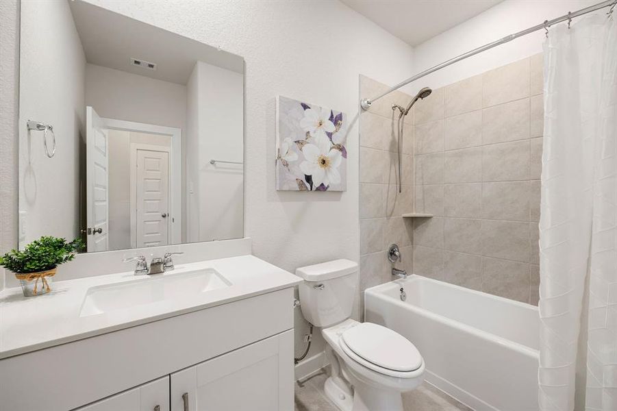 Secondary bathroom features light countertops and cabinets, neutral paint, shower/tub combo with tile surround, large mirror, tile floors, sleek fixtures and modern finishes, plenty of space to accommodate any visiting family or guests.