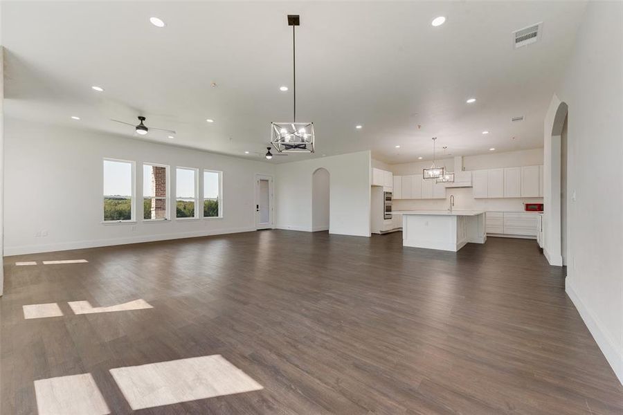 Unfurnished living room with sink, ceiling fan with notable chandelier, and dark hardwood / wood-style flooring