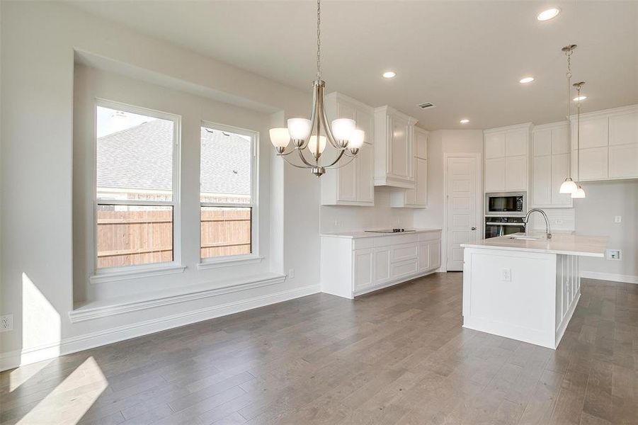 Kitchen with hanging light fixtures, white cabinetry, stainless steel appliances, dark wood-type flooring, and a kitchen island with sink