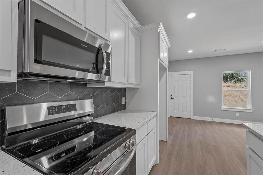 Kitchen with light stone countertops, appliances with stainless steel finishes, white cabinetry, and light hardwood / wood-style floors