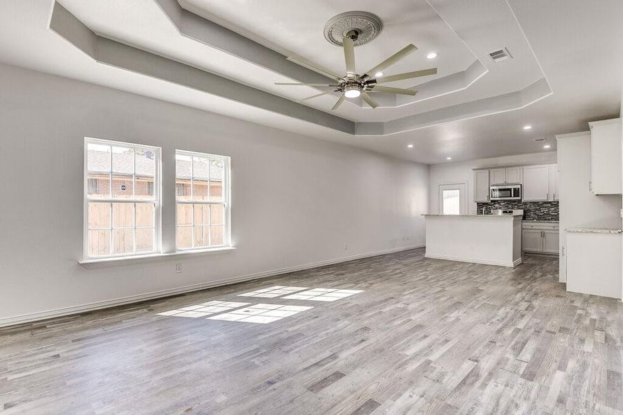 Unfurnished living room featuring ceiling fan, a raised ceiling, and light hardwood / wood-style flooring