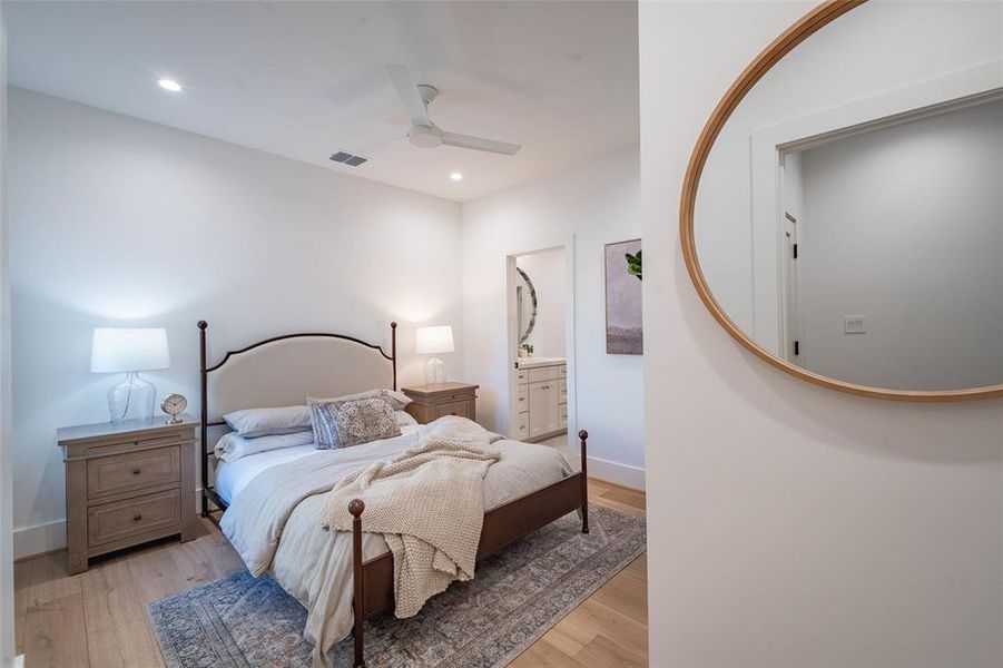 Bedroom with ensuite bath, light hardwood / wood-style floors, and ceiling fan