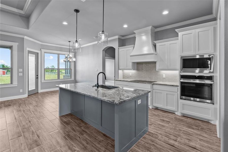 Kitchen featuring white cabinetry, backsplash, premium range hood, stainless steel appliances, and sink