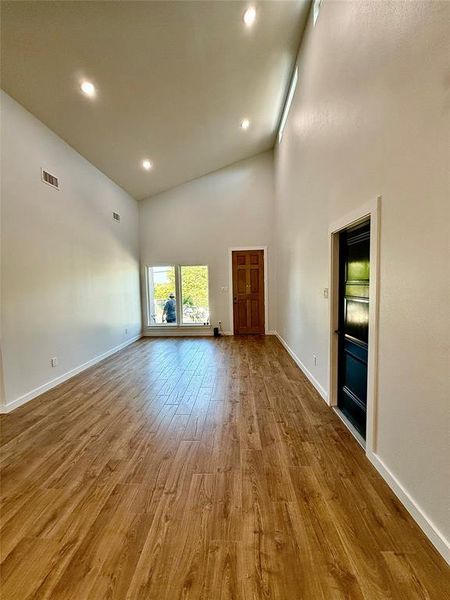 Unfurnished living room with light wood-type flooring and high vaulted ceiling