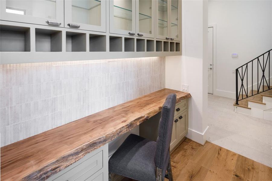 Built-in writing desk with a live edge Sycamore slab, built-in cabinetry with vintage hardware and a pathway leading to the mud room, one of the two utility rooms  and a Three Car garage