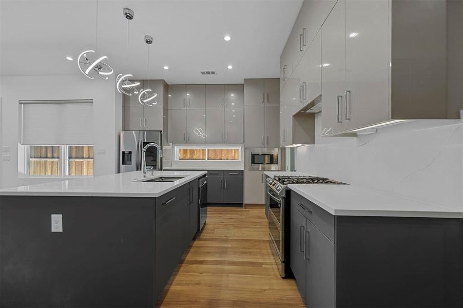 Kitchen featuring a spacious island, pendant lighting, gray cabinets, and stainless steel appliances