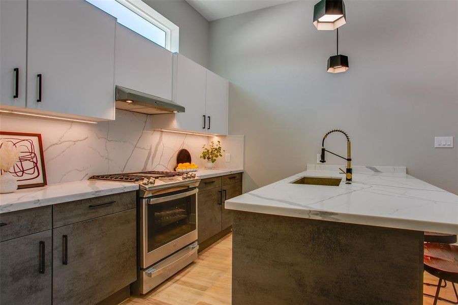 Kitchen with stainless steel gas range oven, light wood-type flooring, wall chimney exhaust hood, decorative light fixtures, and sink