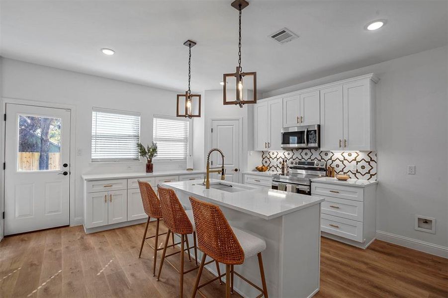 Kitchen featuring appliances with stainless steel finishes, sink, light wood-type flooring, white cabinets, and a kitchen island with sink