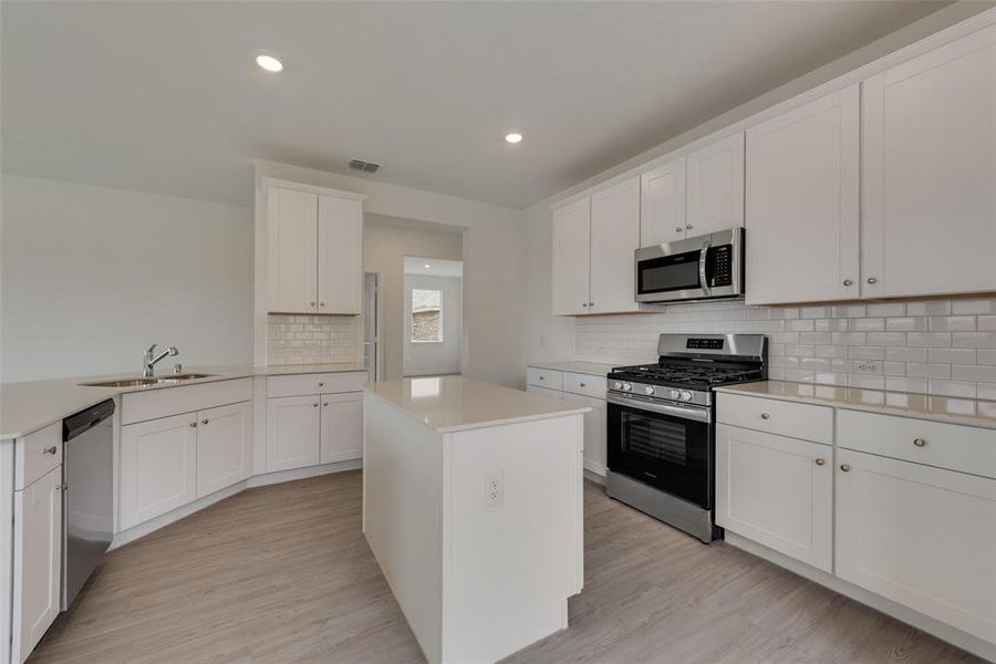 Kitchen featuring stainless steel appliances, white cabinets, sink, a kitchen island, and light hardwood / wood-style floors