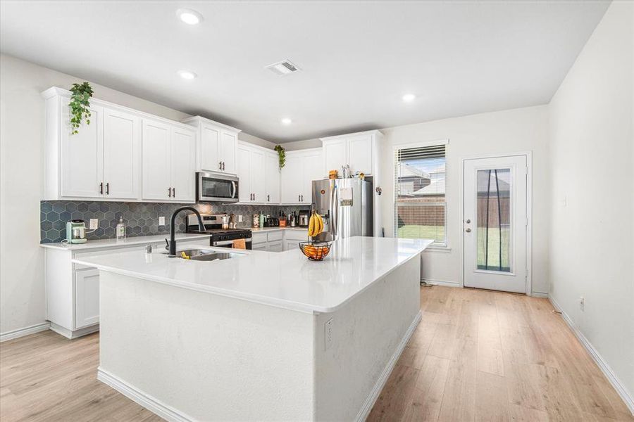 Kitchen featuring light hardwood / wood-style flooring, stainless steel appliances, white cabinets, and a center island with sink