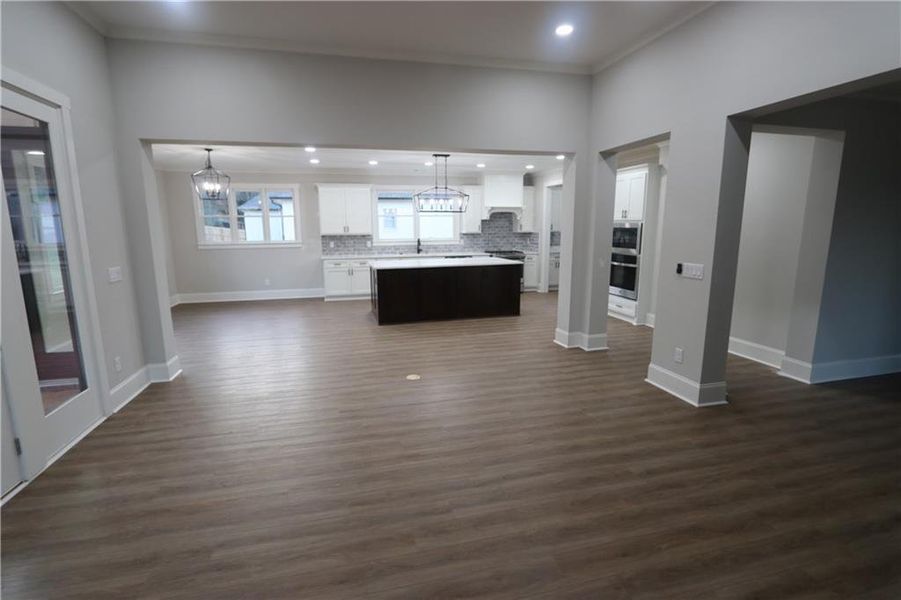 Unfurnished living room with dark hardwood / wood-style floors, crown molding, sink, and a notable chandelier