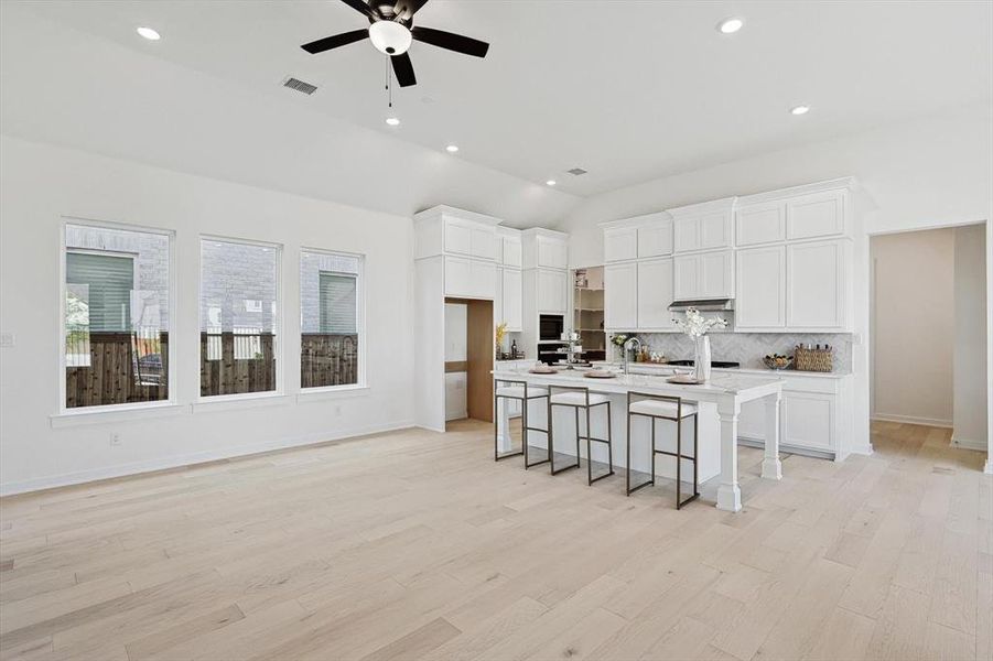 Kitchen featuring light hardwood / wood-style floors, backsplash, a kitchen breakfast bar, ceiling fan, and a kitchen island with sink