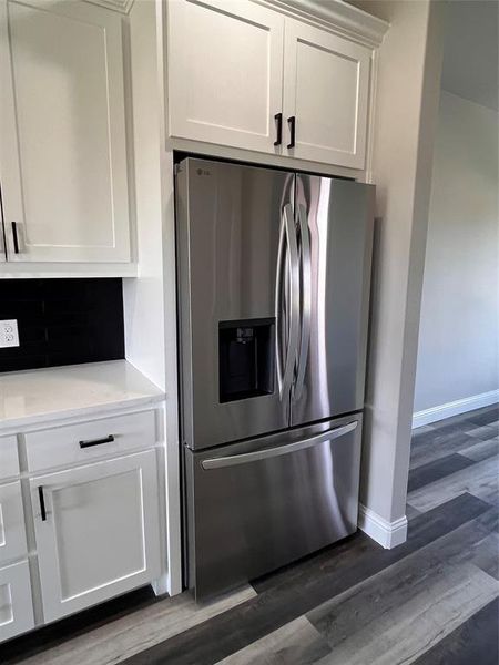 Kitchen with tasteful backsplash, dark hardwood / wood-style flooring, stainless steel fridge with ice dispenser, and white cabinetry