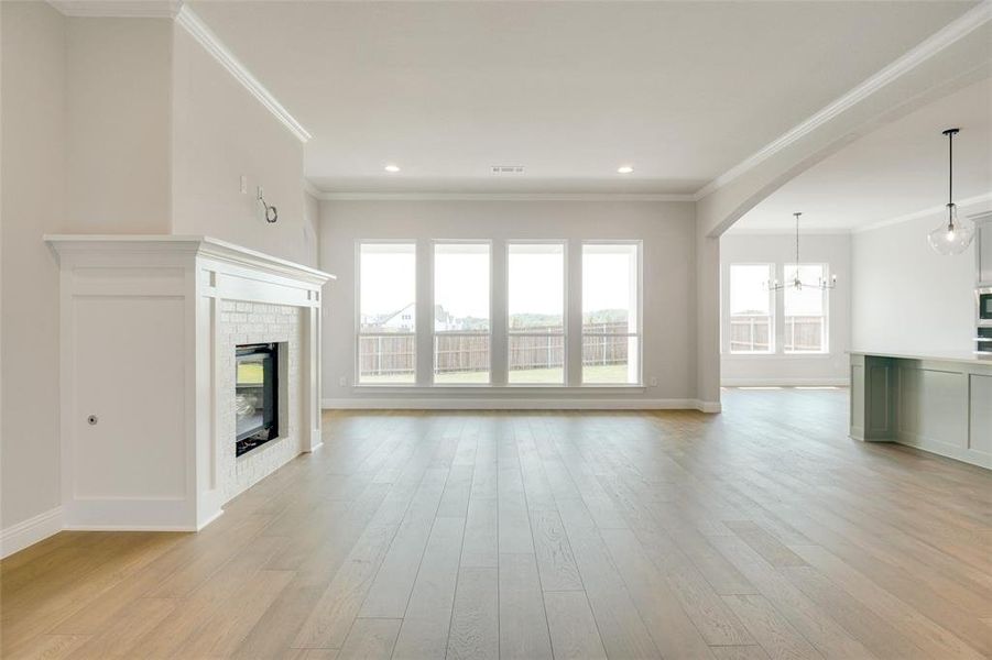 Unfurnished living room featuring crown molding, a brick fireplace, light hardwood / wood-style flooring, and a chandelier