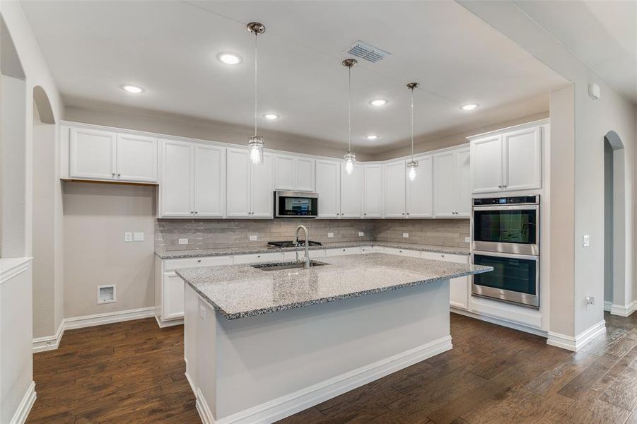 Kitchen with decorative light fixtures, white cabinets, dark wood-type flooring, and stainless steel appliances