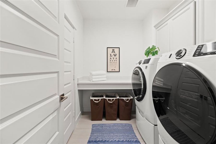 Door From Primary Closet into Laundry Room. Large Folding Table and Overhead Cabinetry.