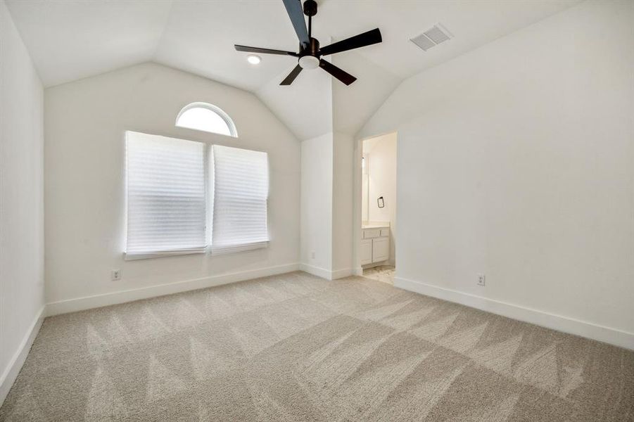 Empty room featuring light colored carpet, ceiling fan, and vaulted ceiling