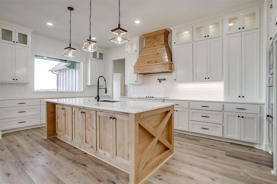 Kitchen with pendant lighting, premium range hood, light hardwood / wood-style floors, an island with sink, and sink