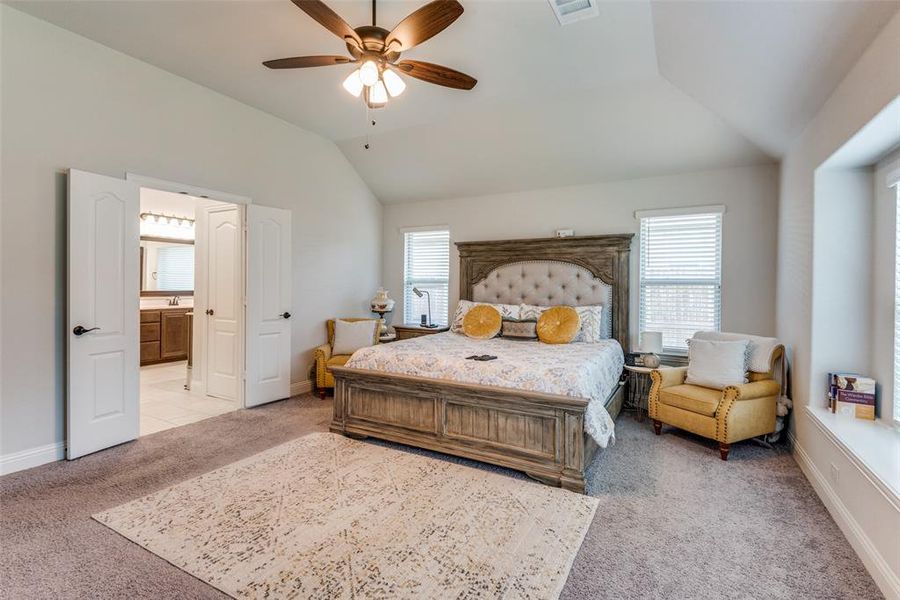 Carpeted bedroom with ceiling fan, lofted ceiling, and ensuite bathroom