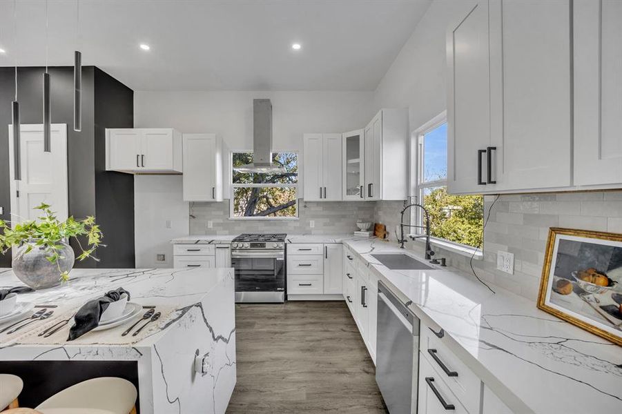 Kitchen with sink, island exhaust hood, plenty of natural light, white cabinetry, and stainless steel appliances