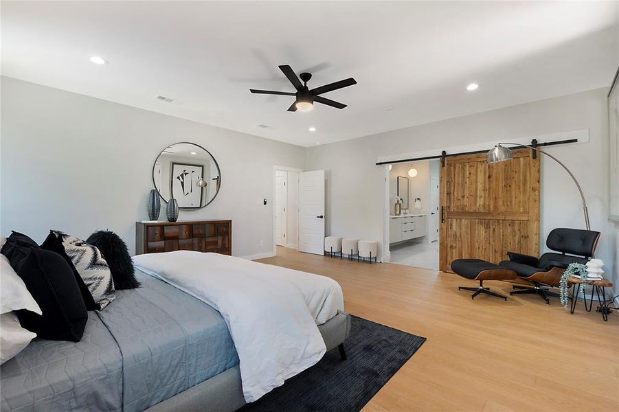 Bedroom featuring ensuite bathroom, a barn door, ceiling fan, and hardwood / wood-style floors