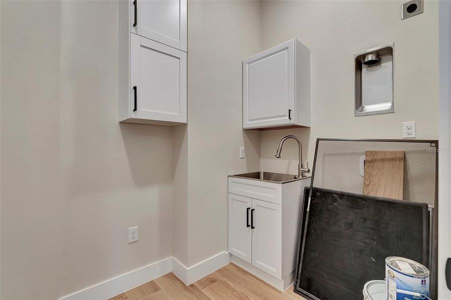 Inside utility room with wash sink, stackable washer and dryer space and tankless water heater incased in double cabinet and plenty of storage space
