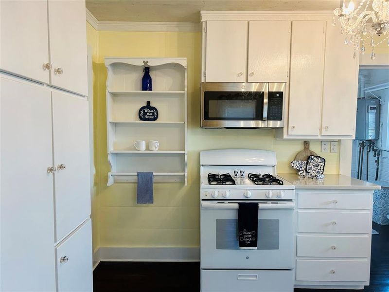 Kitchen with white gas range, dark wood-type flooring, ornamental molding, a notable chandelier, and white cabinets