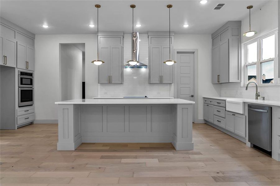 Kitchen featuring light hardwood / wood-style flooring, wall chimney range hood, backsplash, gray cabinets, and stainless steel appliances