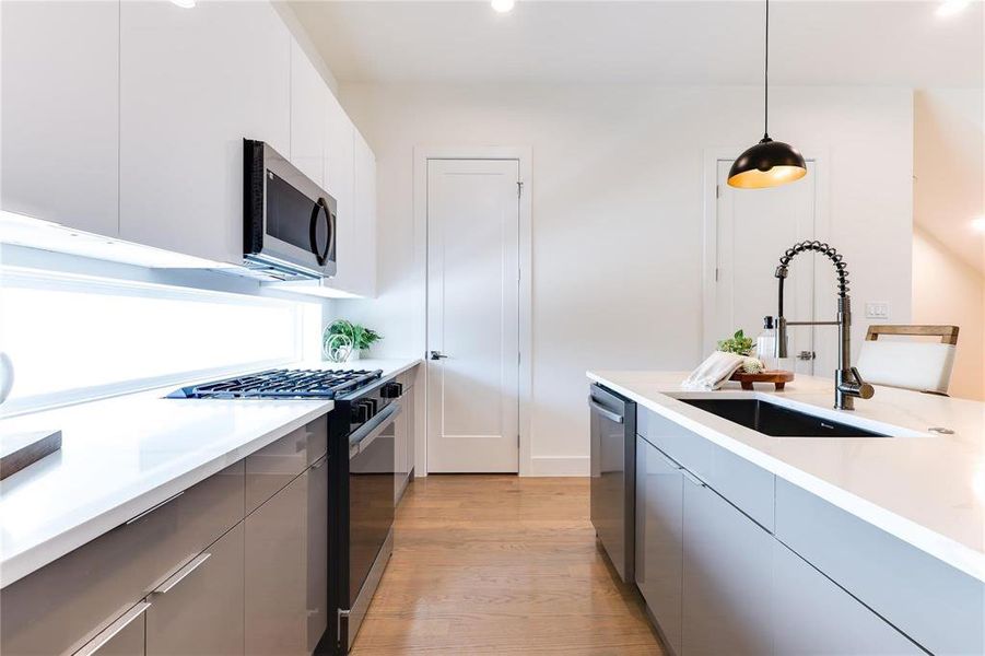 Kitchen featuring appliances with stainless steel finishes, light hardwood / wood-style floors, white cabinets, pendant lighting, and sink