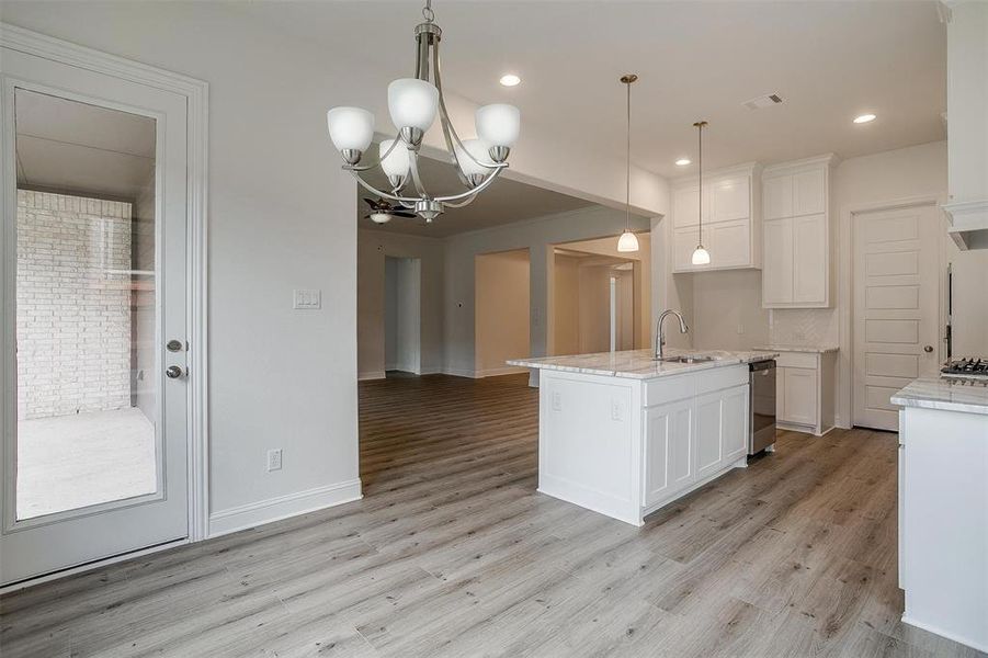 Kitchen with white cabinetry, light hardwood / wood-style flooring, sink, and an island with sink