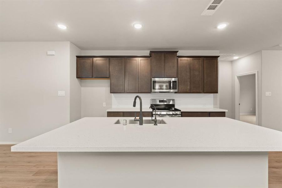 This light and bright kitchen features a large quartz island, dark stained cabinets, a large sink overlooking your family room, recessed lighting, and beautiful backsplash.