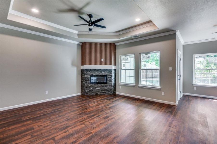 Unfurnished living room featuring a fireplace, dark wood-type flooring, a raised ceiling, and ceiling fan