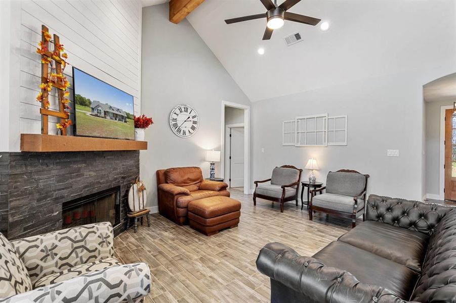 Living room featuring ceiling fan, beamed ceiling, a stone fireplace, high vaulted ceiling, and light wood-type flooring