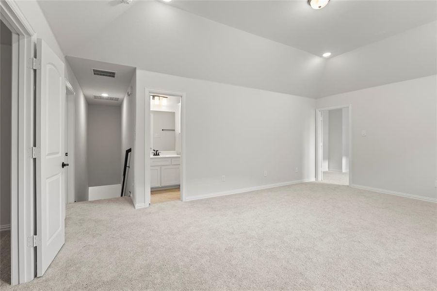 Unfurnished bedroom featuring connected bathroom, light colored carpet, and vaulted ceiling