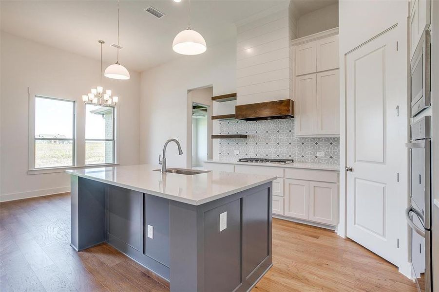 Kitchen with light hardwood / wood-style flooring, an island with sink, white cabinets, sink, and tasteful backsplash