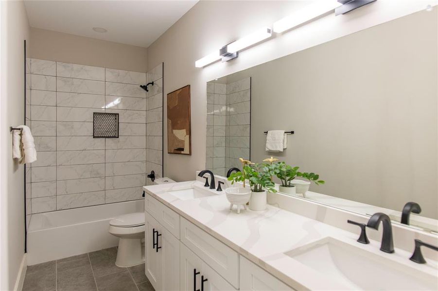 Full bathroom featuring tile flooring, double sink, tiled shower / bath, vanity with extensive cabinet space, and toilet