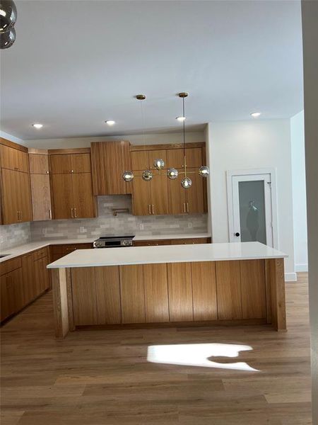 Kitchen with a spacious island, hardwood / wood-style floors, high end stove, and hanging light fixtures