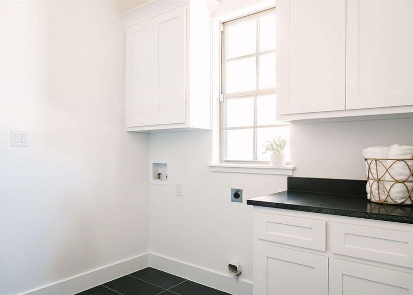 Laundry room with hookup for an electric dryer, hookup for a washing machine, dark tile patterned flooring, and a wealth of natural light