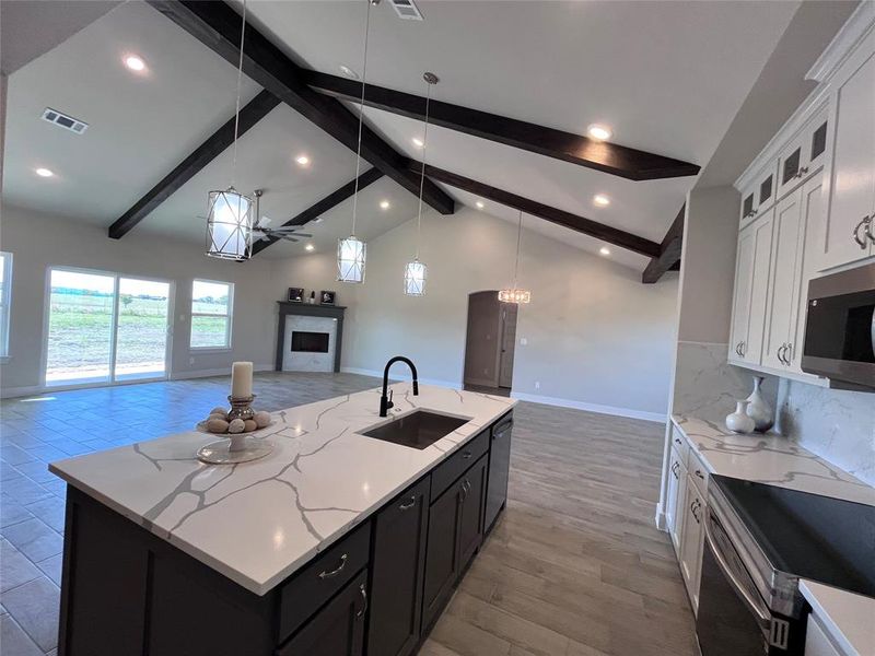 Kitchen with sink, beamed ceiling, an island with sink, and white cabinets