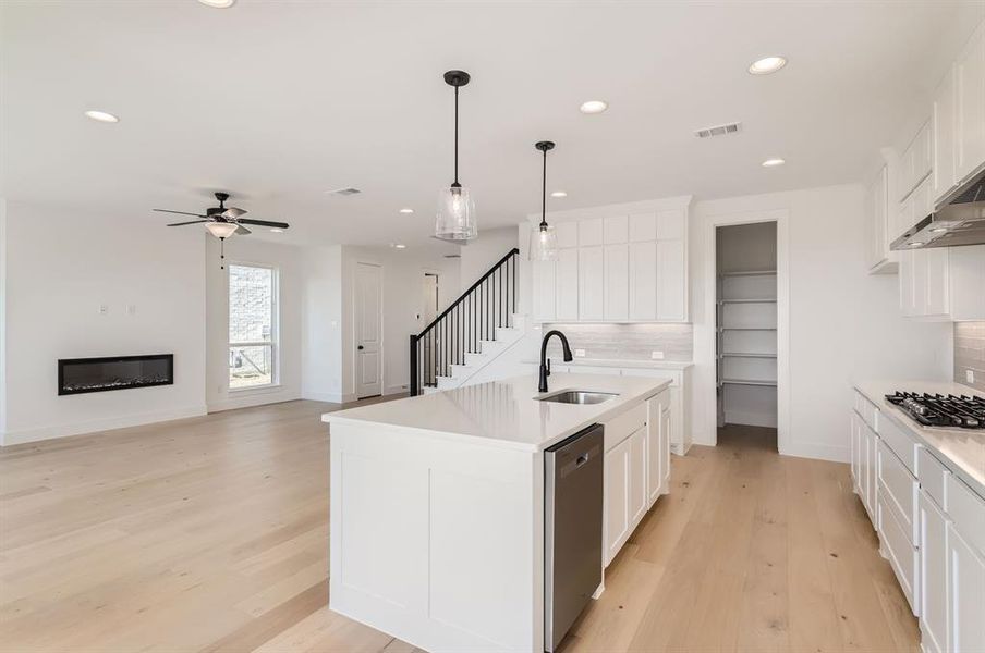 Kitchen with tasteful backsplash, appliances with stainless steel finishes, white cabinetry, a kitchen island with sink, and sink