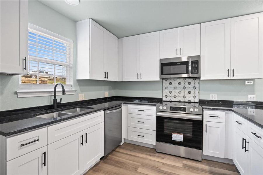 Kitchen featuring appliances with stainless steel finishes, white cabinetry, hardwood / wood-style flooring, and sink