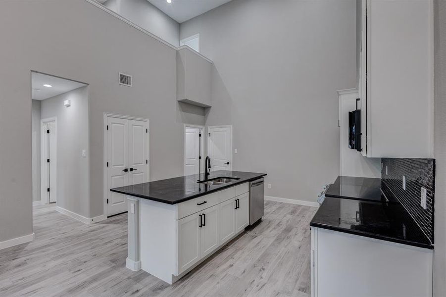 Kitchen featuring stainless steel dishwasher, white cabinets, light wood-type flooring, sink, and a towering ceiling