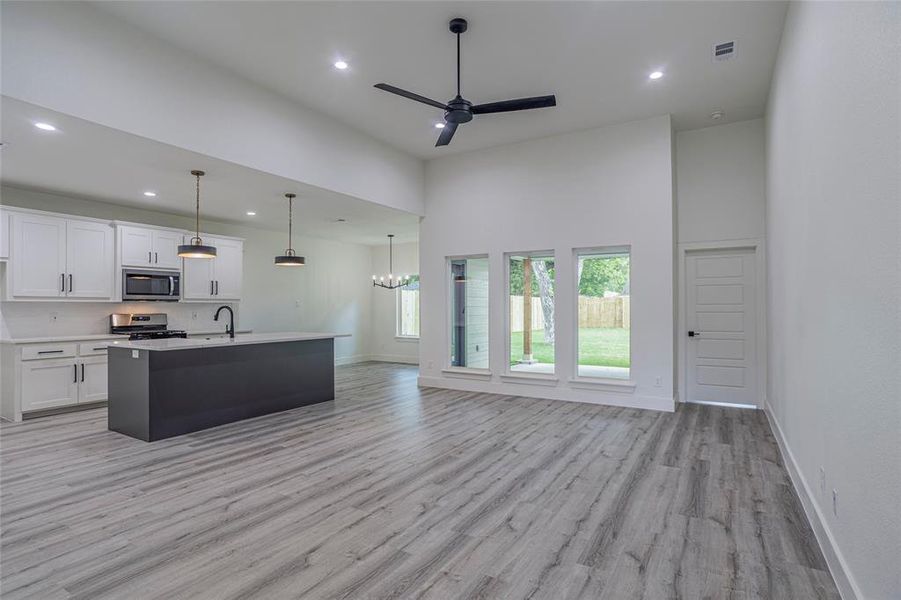 Kitchen featuring stainless steel appliances, sink, a high ceiling, light wood-type flooring, and white cabinetry