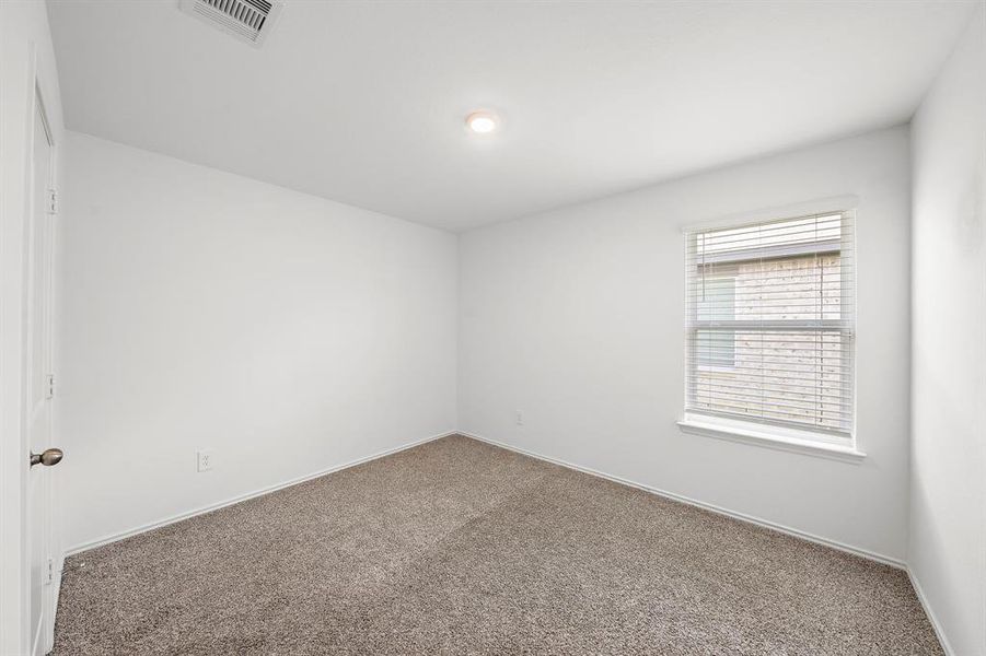 The spacious secondary bedroom features fresh white walls, a large window with blinds for natural light, and plush carpeting—a great blank canvas for personalization.