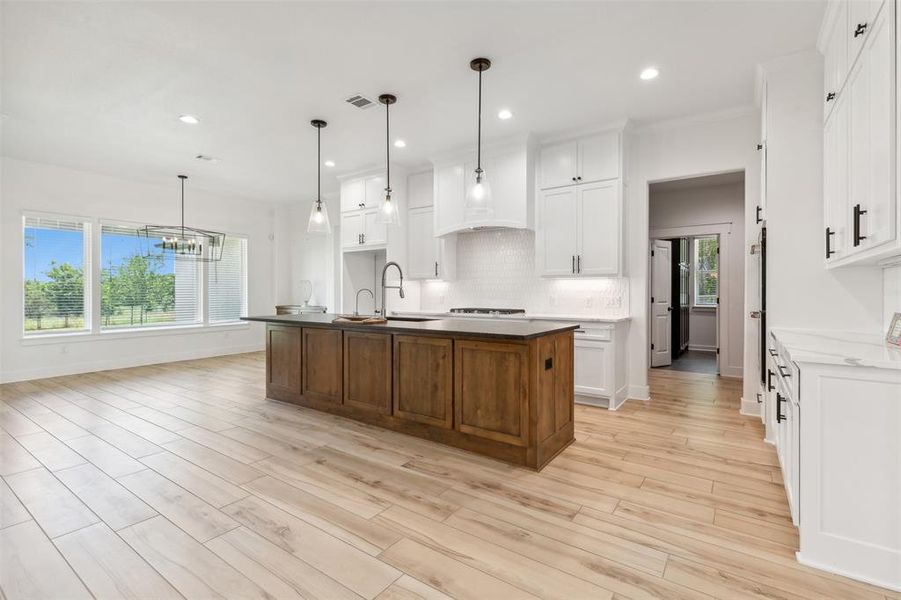 Kitchen with white cabinetry, light hardwood / wood-style flooring, a kitchen island with sink, backsplash, and pendant lighting