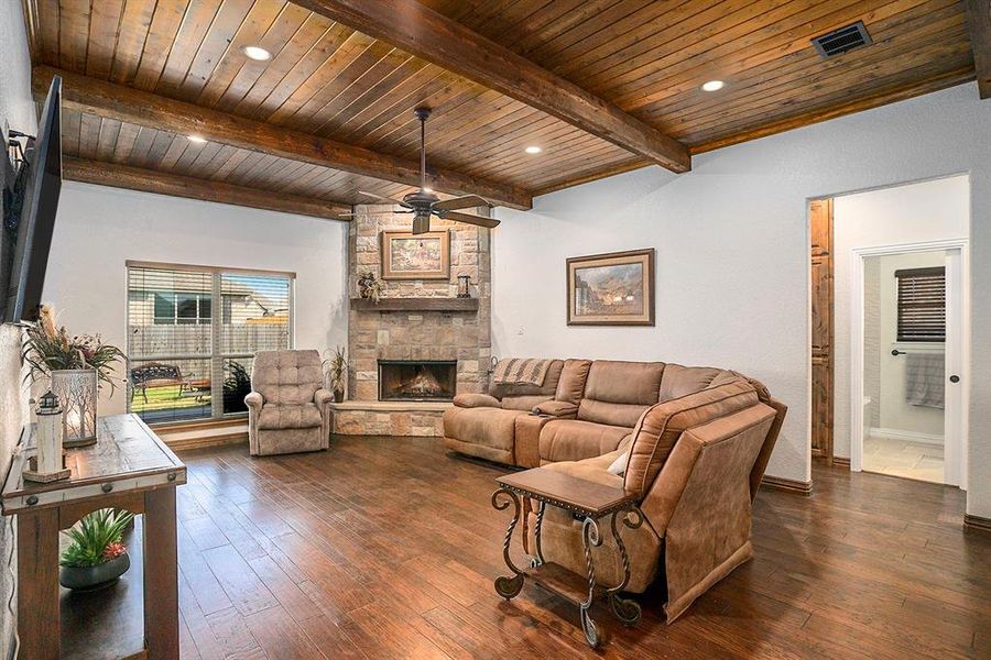 Living room with beamed ceiling, dark wood-type flooring, wooden ceiling, a fireplace, and ceiling fan